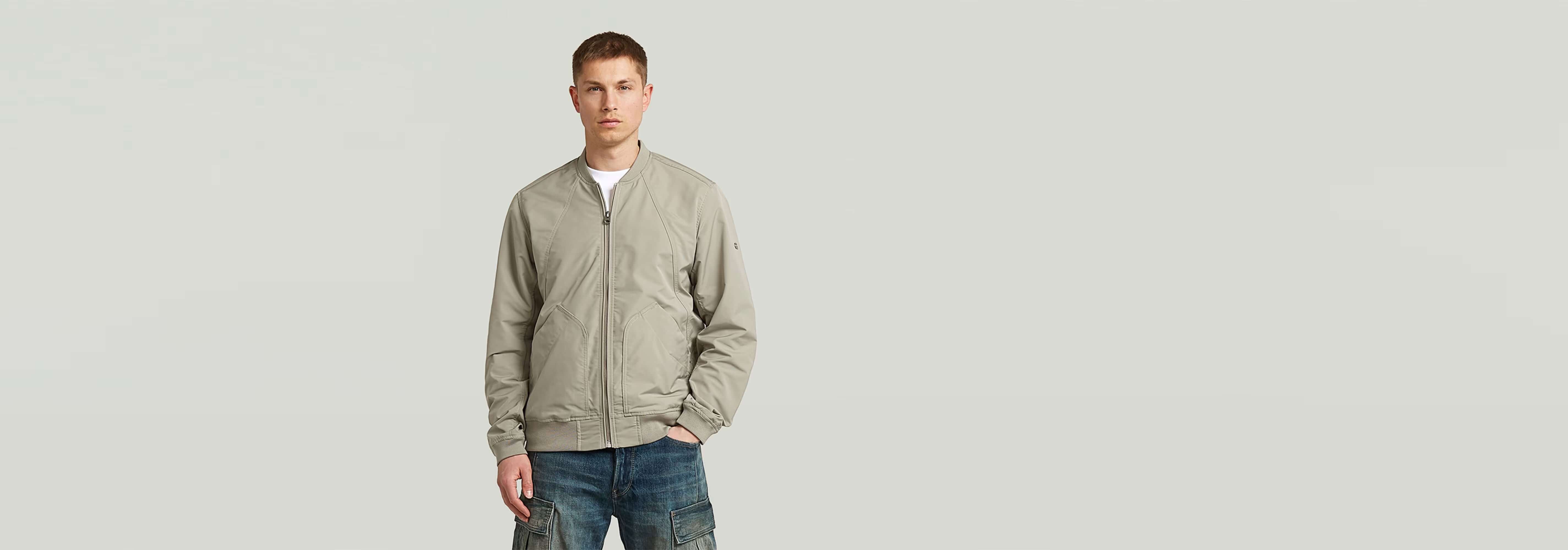 Hombre con chaqueta bomber sin acolchado, de corte recto, en color gris, mostrando bolsillos y cierre de cremallera.