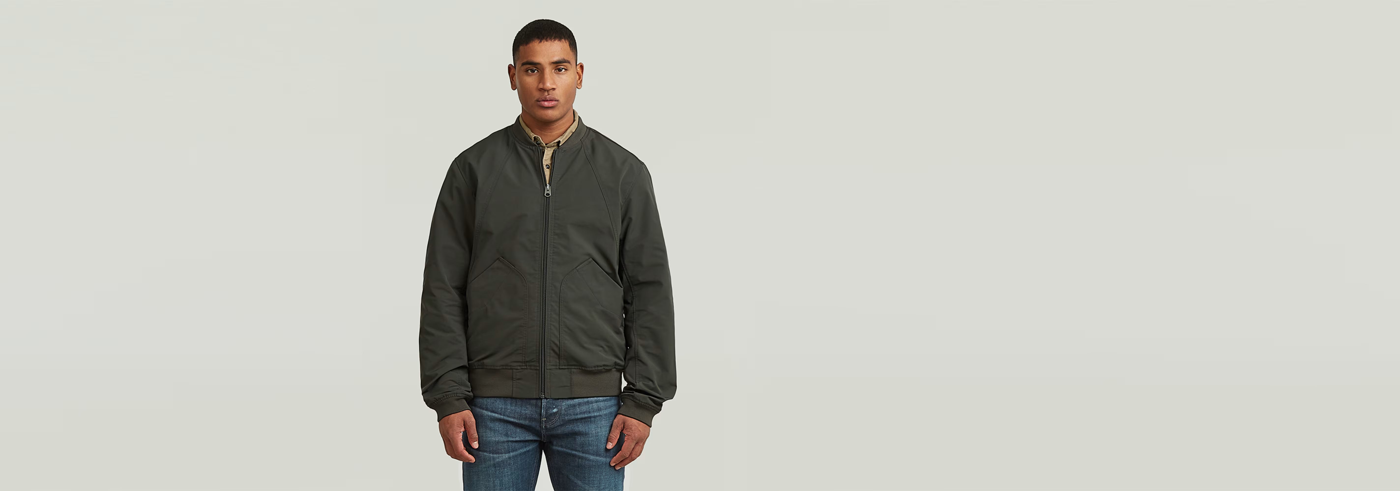Hombre vistiendo chaqueta bomber unpadded de corte recto en color oscuro, frente a fondo claro.