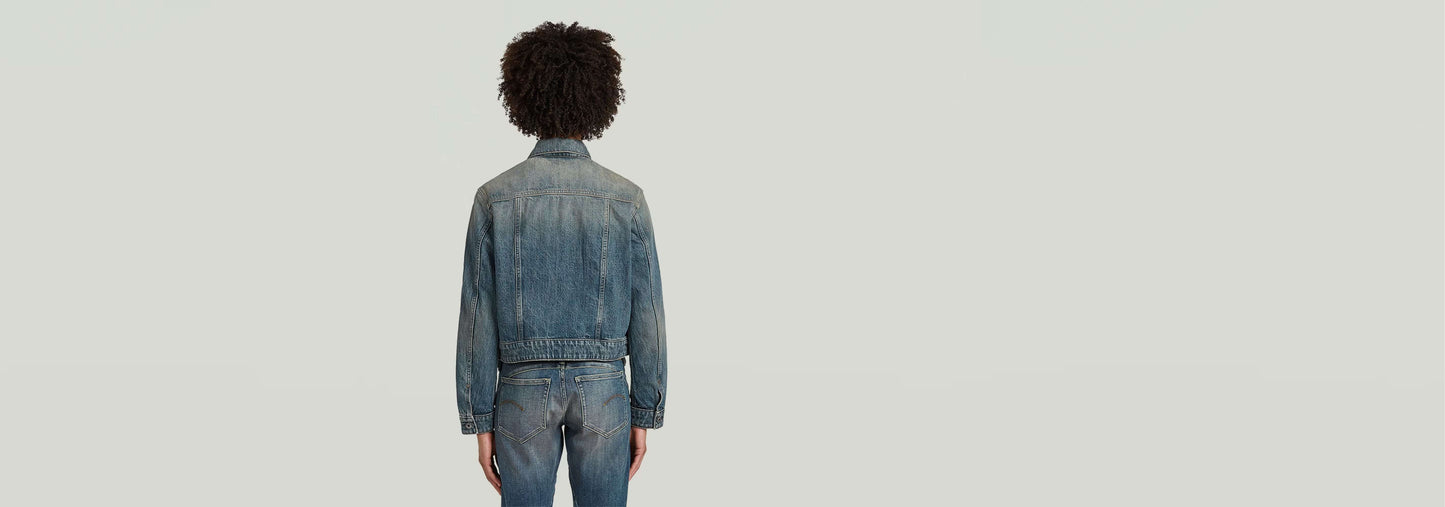 Vista posterior de una persona usando una chaqueta encogida Boxy en denim greencast con tinte índigo.
