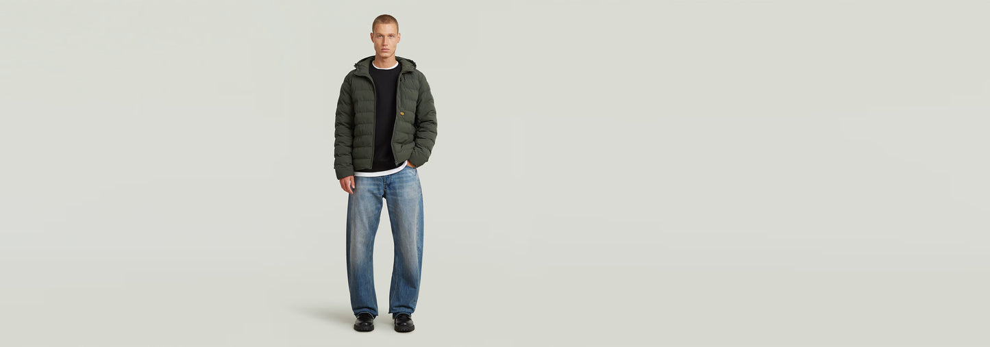 Modelo usando la chaqueta Foundation Hooded Liner con jeans, mostrando el diseño acolchado y la capucha.
