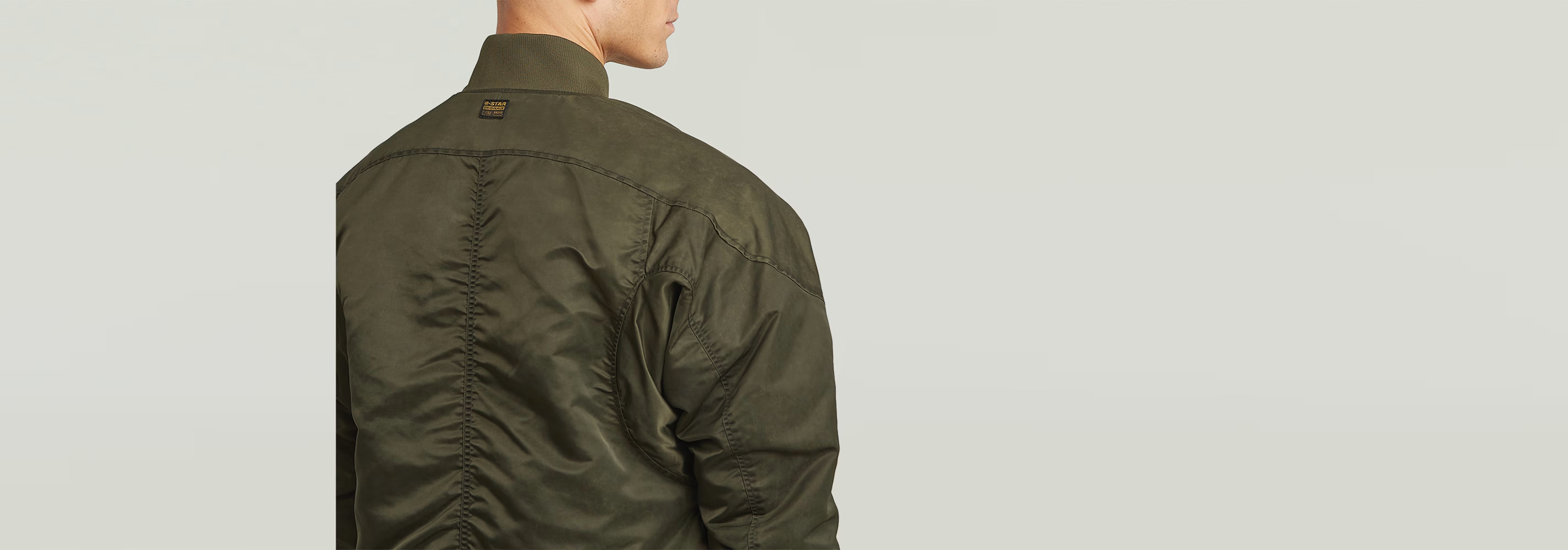 Hombre usando la chaqueta GA-1 Lightweight Padded Bomber desde atrás, mostrando el diseño acolchado y el color verde.