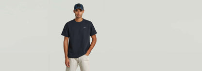 Hombre modelando una gorra de rejilla Baseball con camiseta oscura y pantalones claros en fondo neutro.