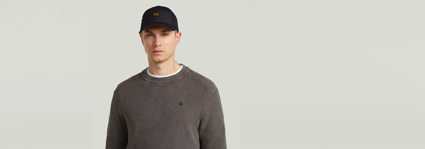 Hombre modelando una gorra Originals Baseball negra con visera curvada y logotipo bordado en fondo claro.