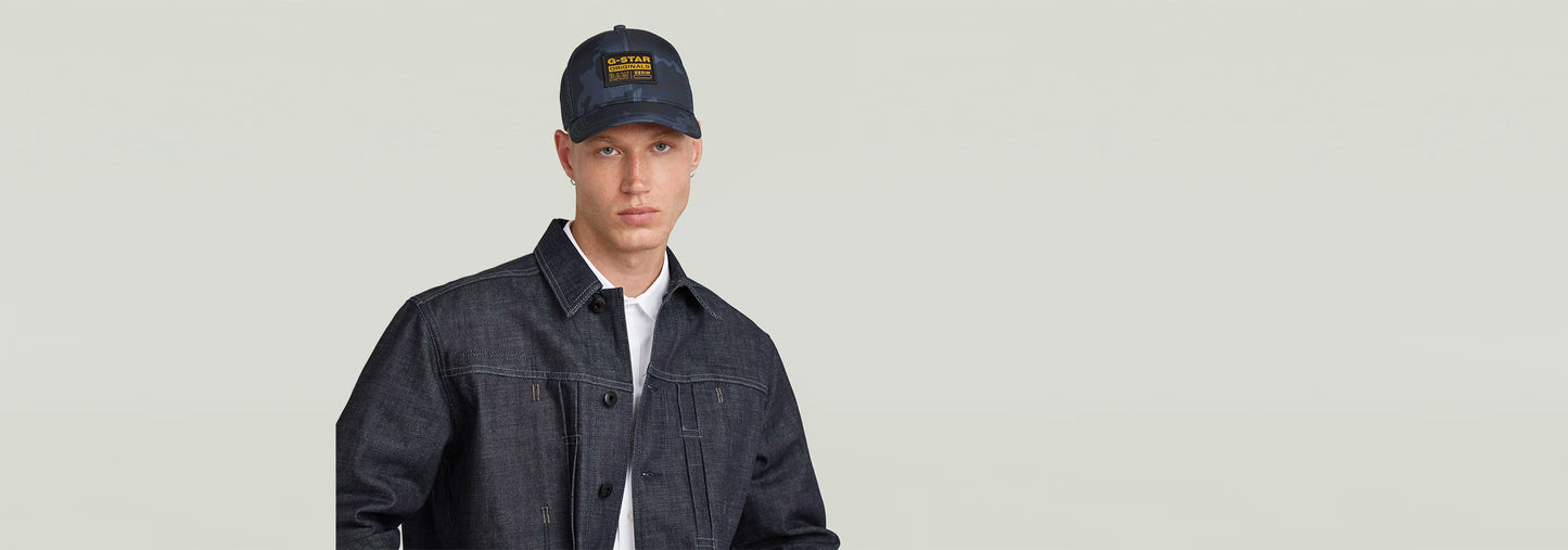 Modelo vistiendo gorra unisex Baseball Trucker con chaqueta de mezclilla y fondo claro.