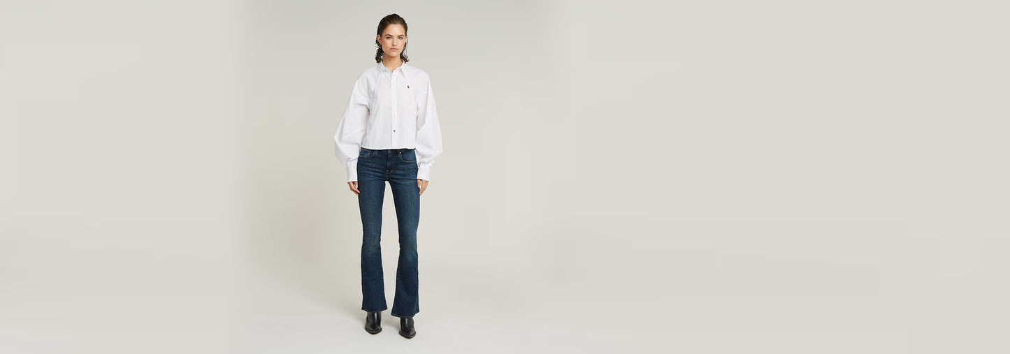 Mujer vistiendo Jeans 3301 Flare en color azul con blusa blanca, pose de pie.