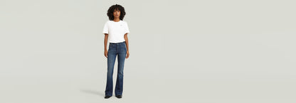 Mujer usando Jeans 3301 Flare con camiseta blanca, estilo años 70, en fondo claro.