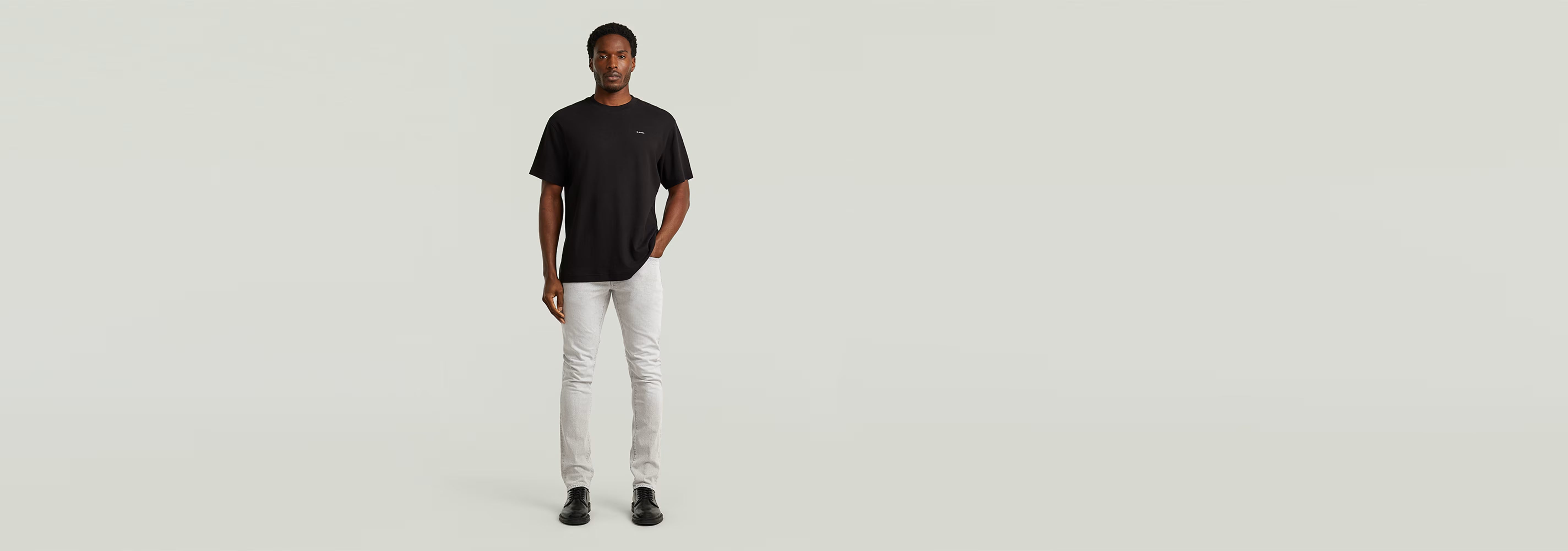 Hombre luciendo Jeans 3301 Slim, con corte ajustado y diseño clásico, camiseta negra y fondo minimalista.