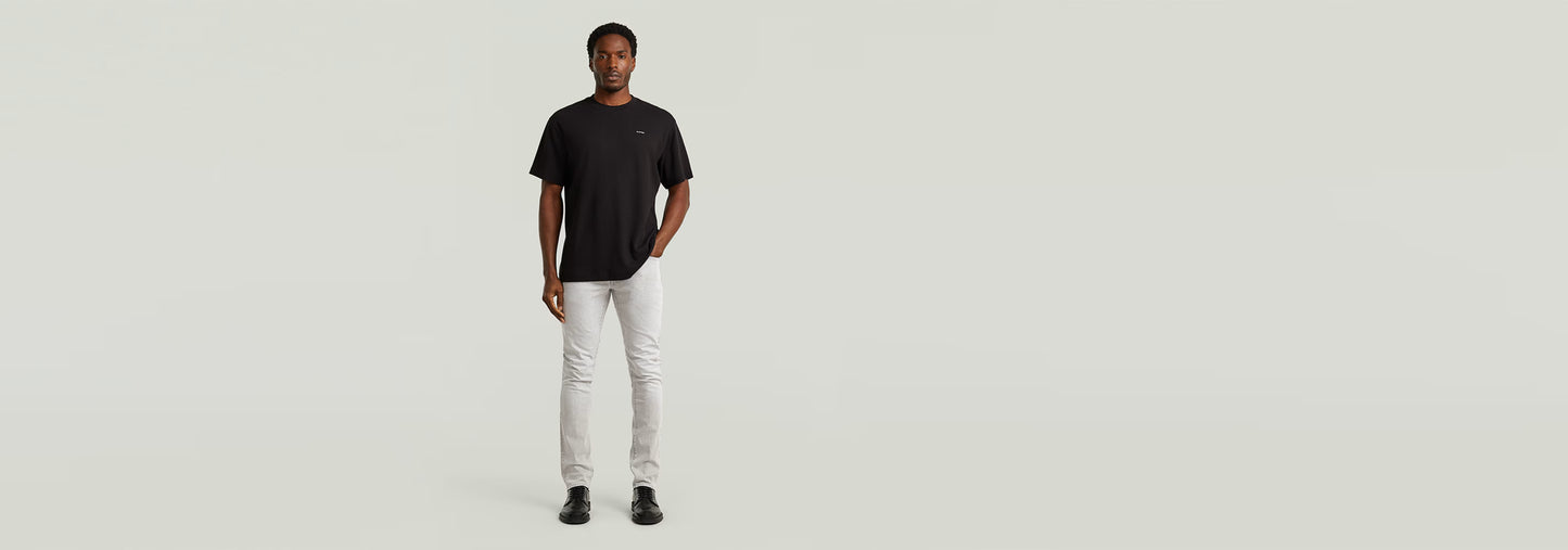 Hombre luciendo Jeans 3301 Slim, con corte ajustado y diseño clásico, camiseta negra y fondo minimalista.