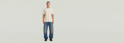 Modelo usando Jeans Bend Loose y camiseta beige en fondo claro, resaltando el estilo moderno de la colección Anatomic Denim.