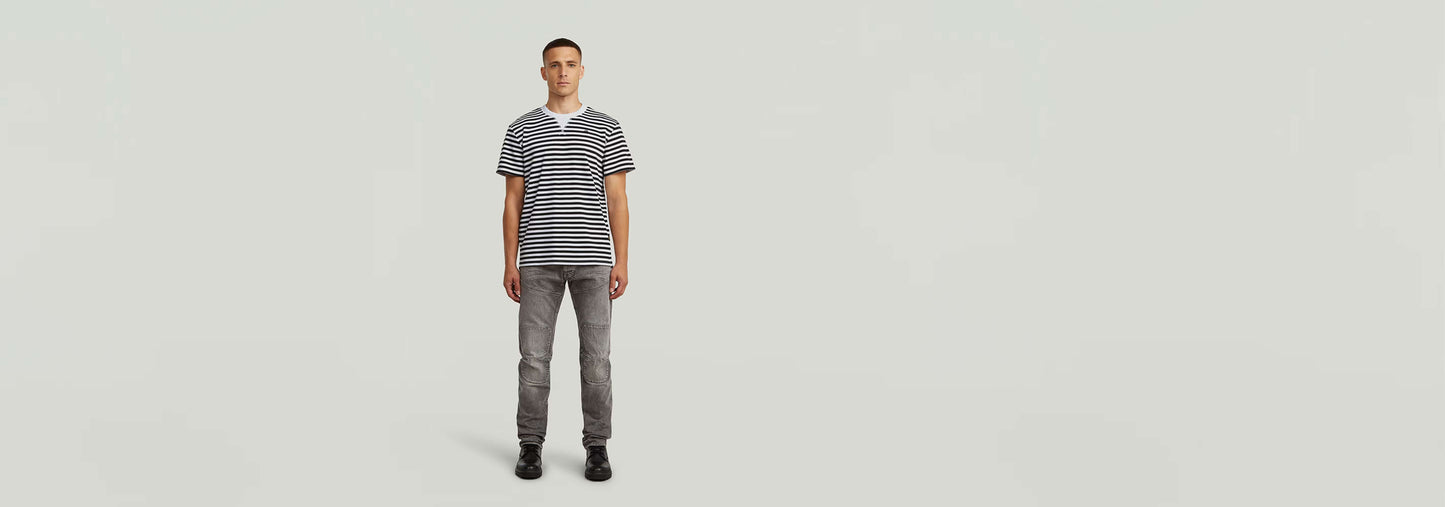 Modelo luciendo Jeans Biker Patched Slim con camiseta de rayas en fondo neutro.