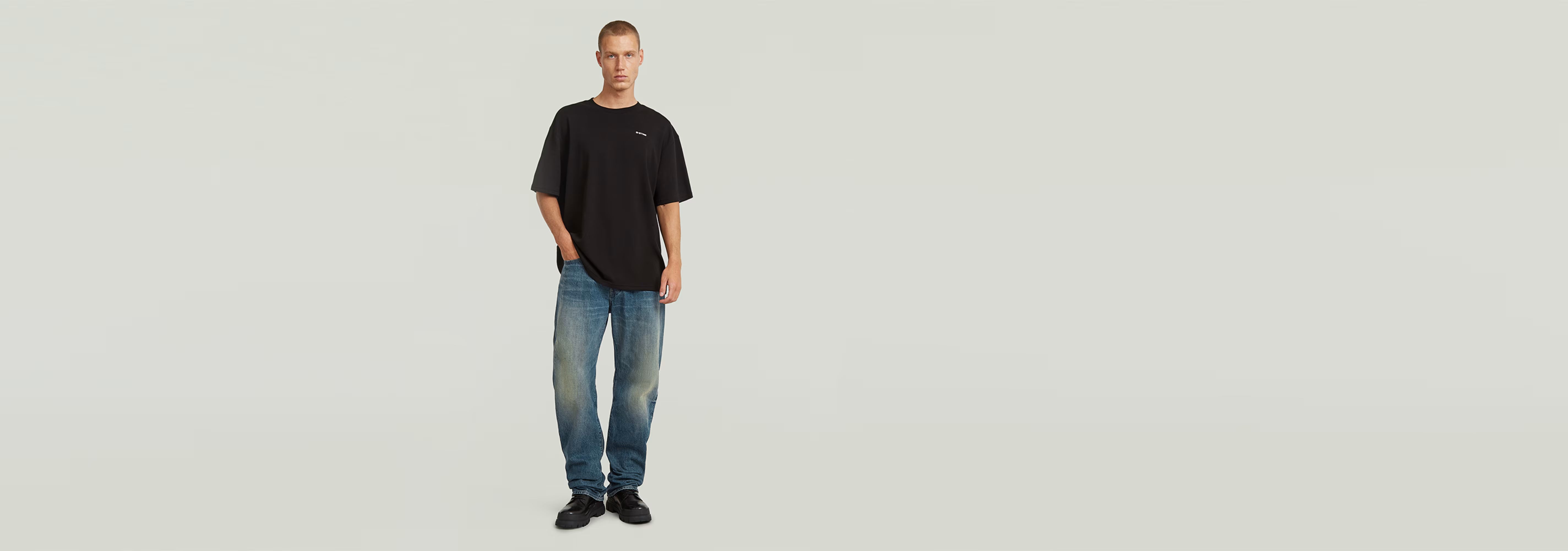 Hombre usando Jeans Contor Regular con camiseta negra y zapatos oscuros en fondo claro.