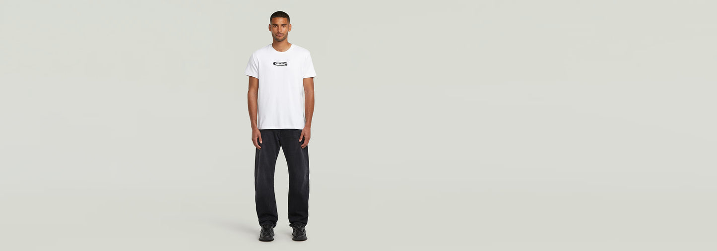 Modelo masculino vistiendo una camiseta blanca y pantalones oscuros, con logo en la parte frontal.