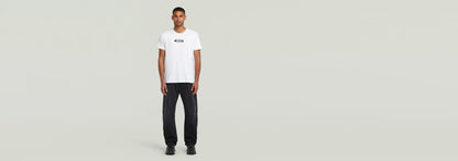 Modelo masculino vistiendo una camiseta blanca y pantalones oscuros, con logo en la parte frontal.