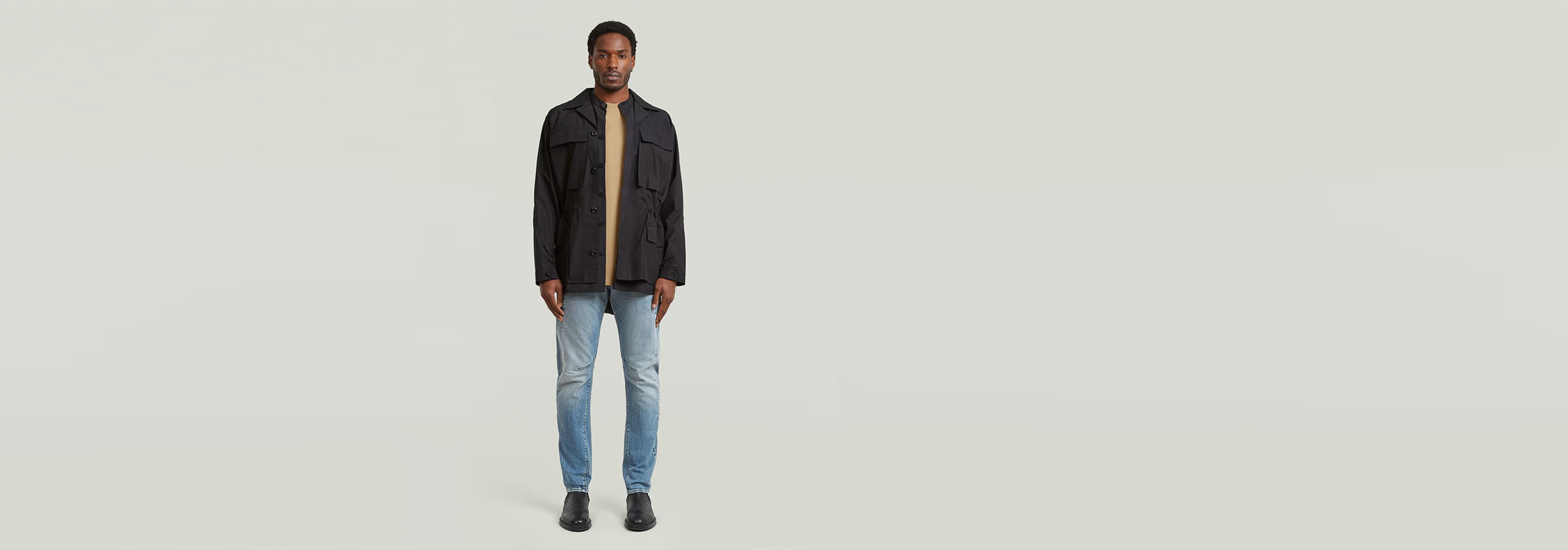 Hombre usando jeans Contor Slim con chaqueta negra y camiseta, de pie sobre fondo claro.