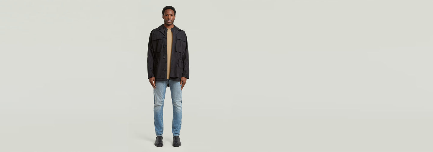 Hombre usando jeans Contor Slim con chaqueta negra y camiseta, de pie sobre fondo claro.