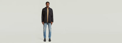 Hombre usando jeans Contor Slim con chaqueta negra y camiseta, de pie sobre fondo claro.