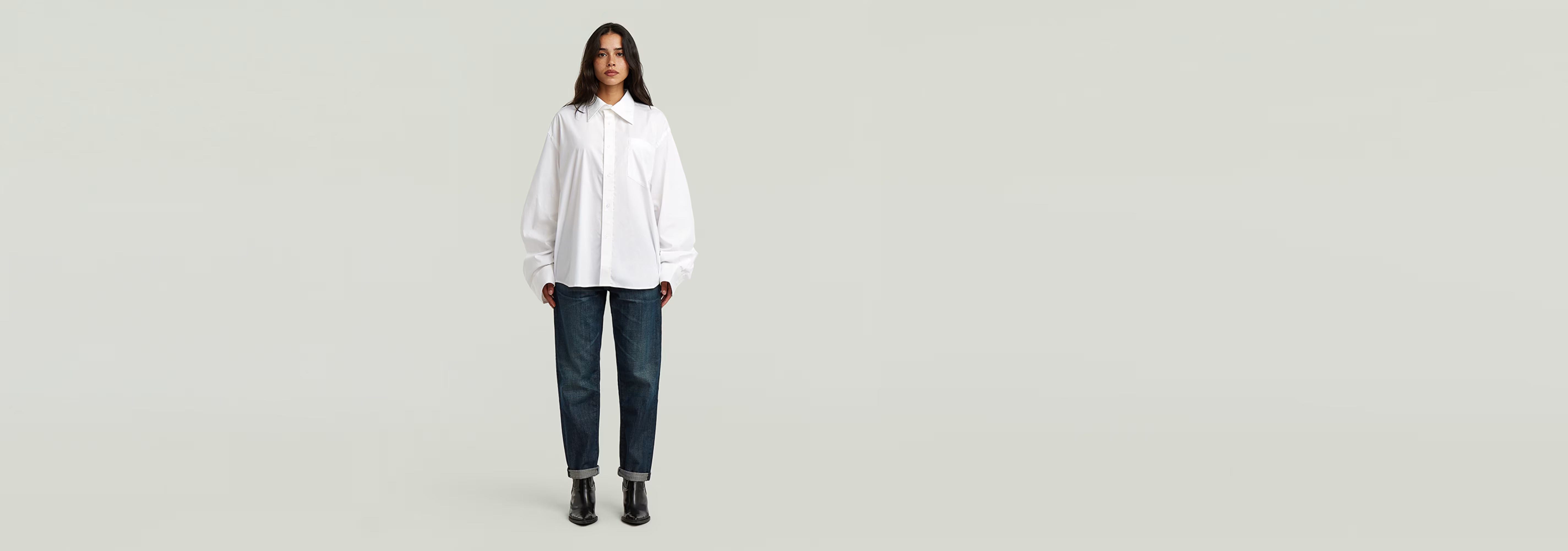 Mujer usando Jeans Kate Boyfriend con camisa blanca y botas negras sobre fondo claro.
