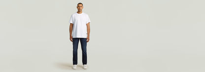 Modelo vistiendo Jeans Mosa Straight en un fondo neutro con camiseta blanca y zapatillas. Moda masculina.