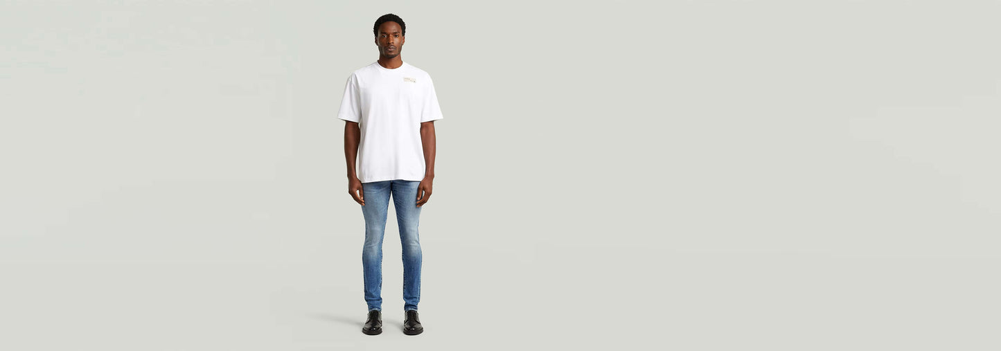 Hombre usando Jeans Revend FWD Skinny con camiseta blanca, en un fondo neutral, mostrando el corte pitillo.