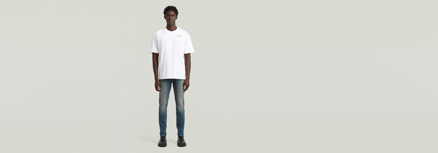 Hombre usando Jeans Revend FWD Skinny con camiseta blanca frente a fondo claro.