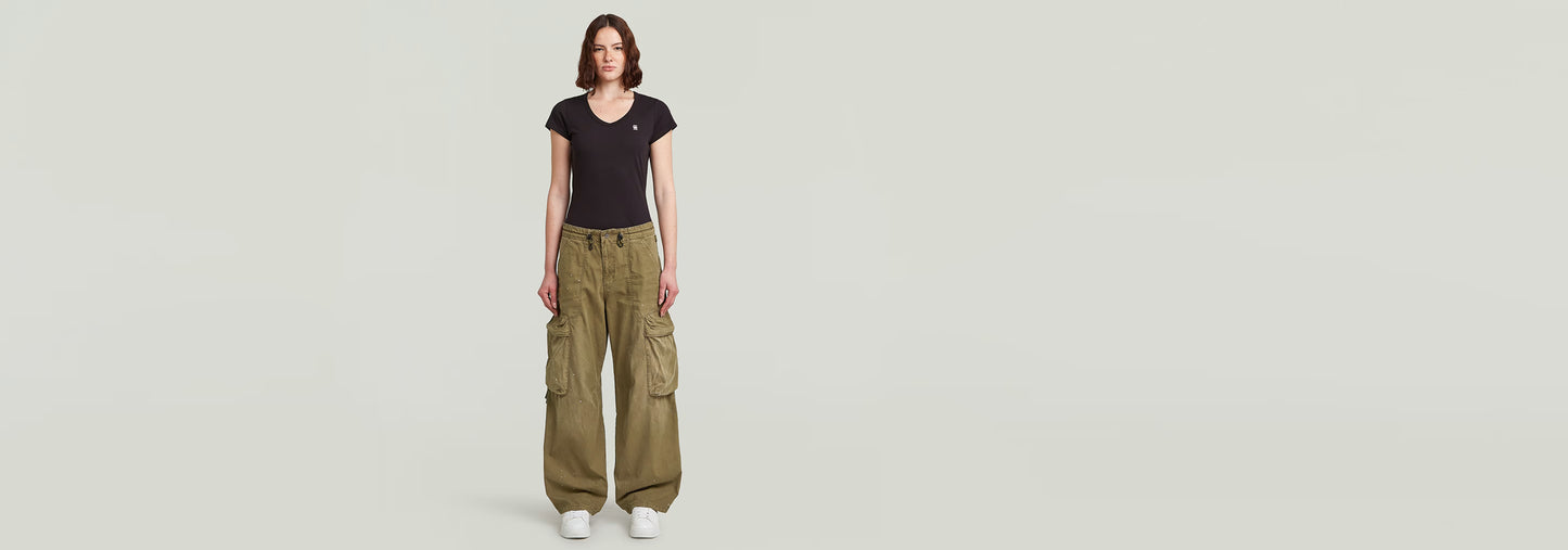 Modelo usando Pantalones Balloon Cargo de corte cónico en color verde con camiseta negra de fondo blanco.