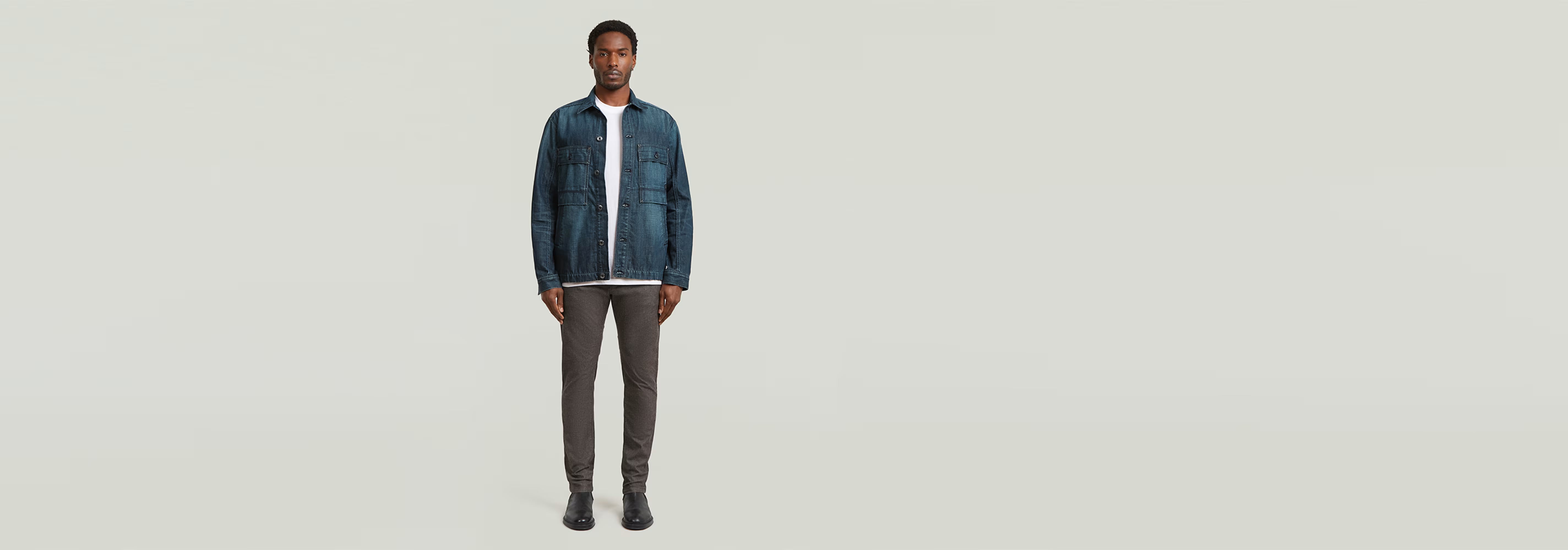 Modelo usando Pantalones Bronson 3.0 Slim Chino con chaqueta denim, fondo claro, estilo casual.