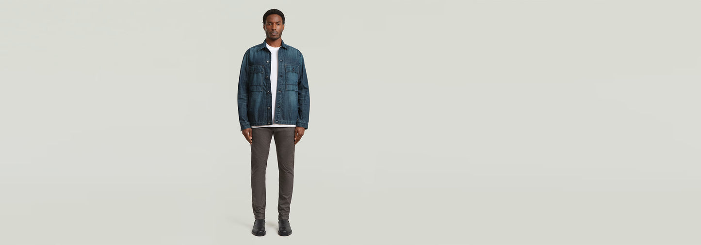 Modelo usando Pantalones Bronson 3.0 Slim Chino con chaqueta denim, fondo claro, estilo casual.