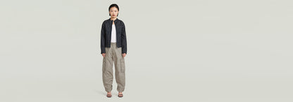 Mujer vistiendo pantalones cargo 3D Boyfriend con chaqueta negra y blusa blanca en fondo neutro.