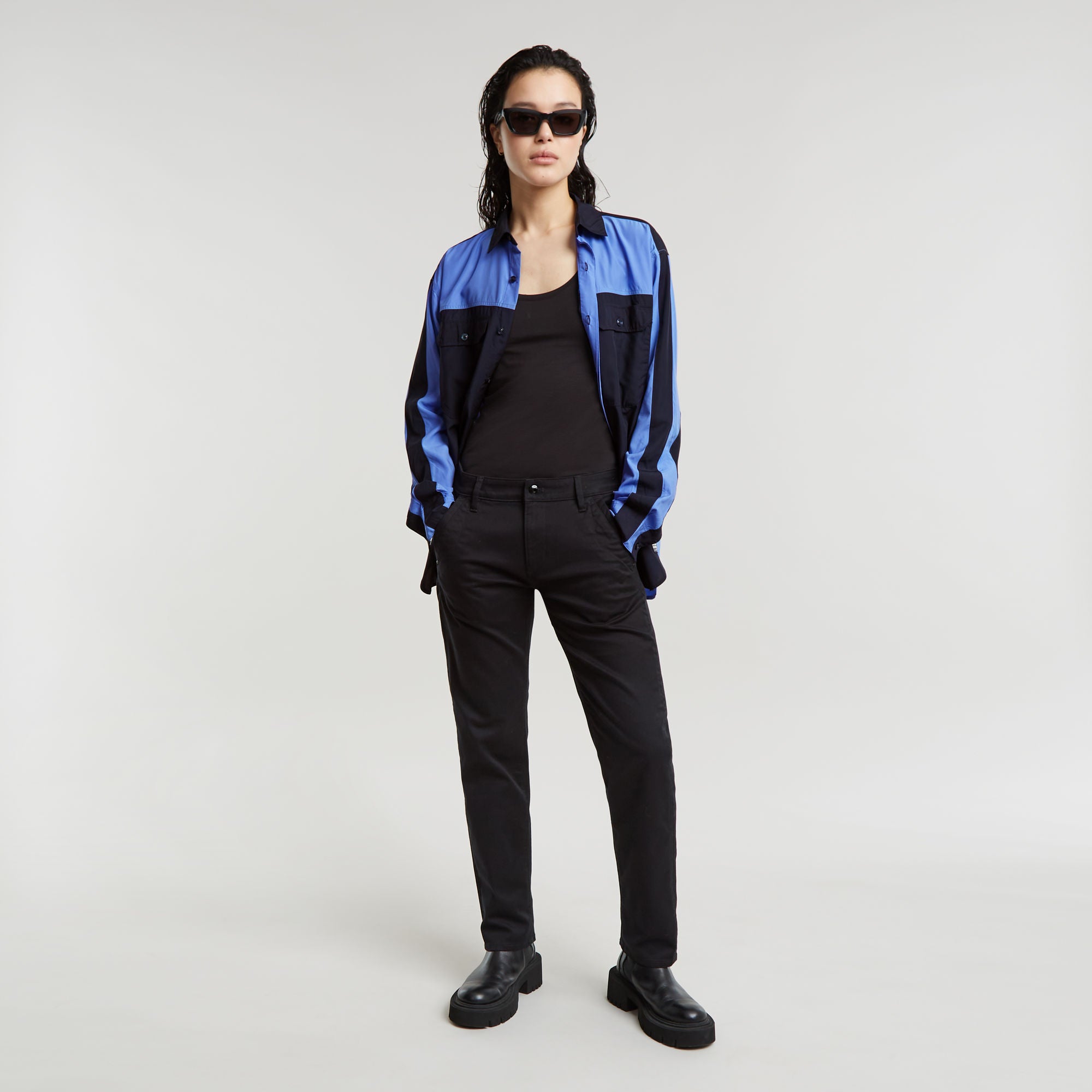 Modelo luciendo pantalones boyfriend Kate con camisa azul y gafas de sol, fondo claro.