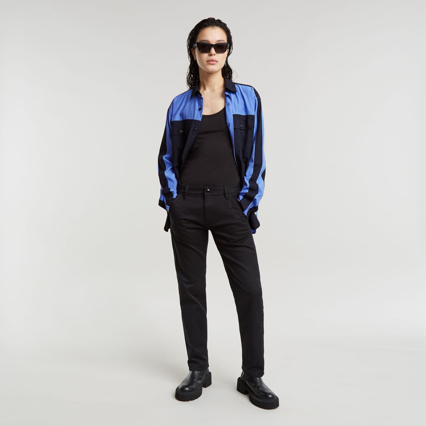 Modelo luciendo pantalones boyfriend Kate con camisa azul y gafas de sol, fondo claro.