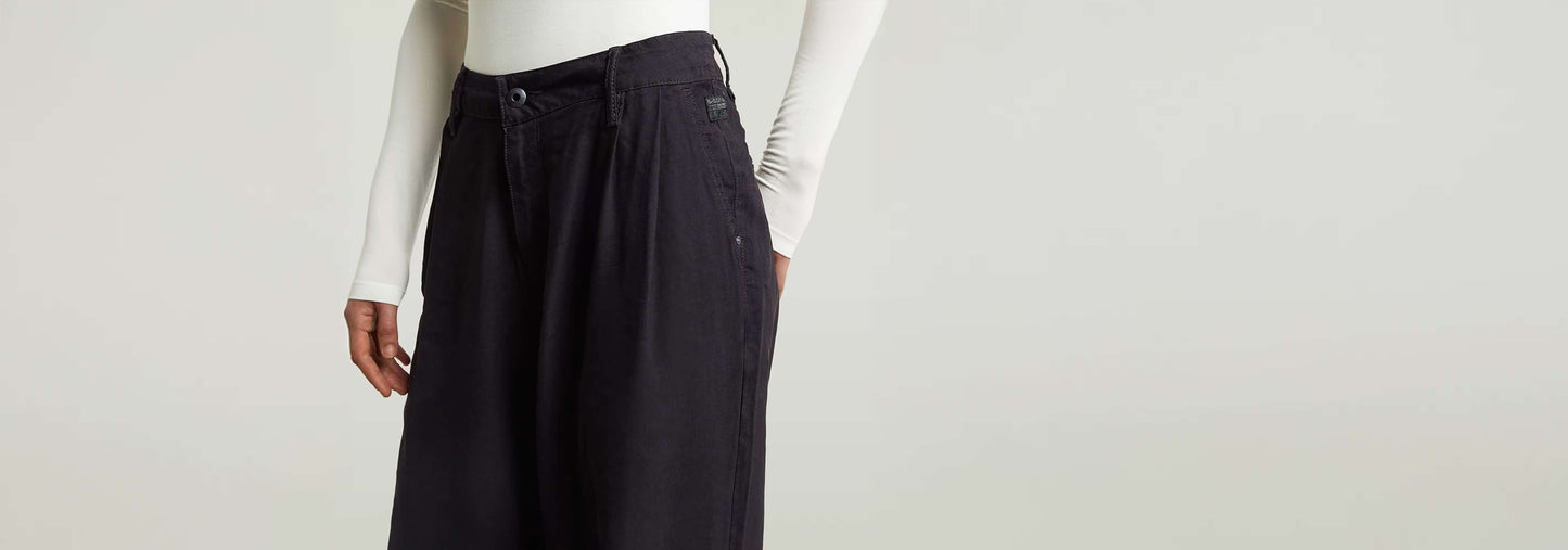 Pantalones Pleated Chino con un diseño plisado y ajuste recto, mostrando cierre de cremallera y bolsillos.
