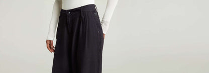 Pantalones Pleated Chino con un diseño plisado y ajuste recto, mostrando cierre de cremallera y bolsillos.