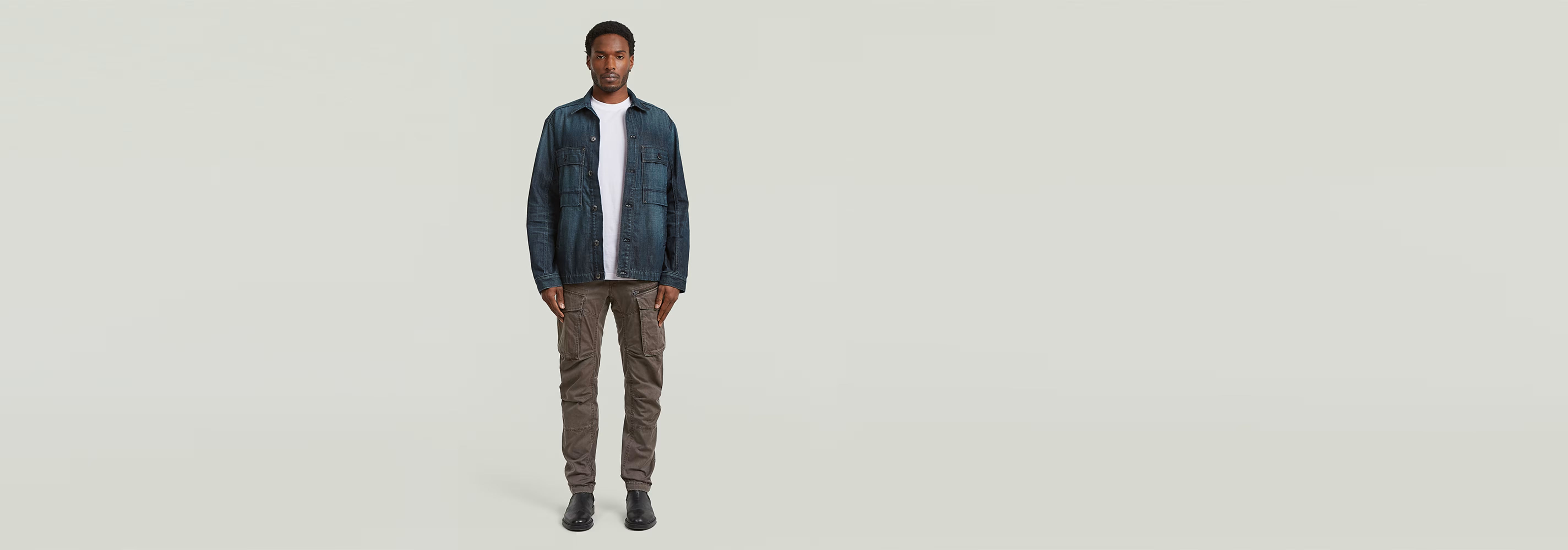 Modelo con Pantalones Rovic Zip 3D Regular Tapered, camiseta blanca y chaqueta azul, de pie sobre fondo claro.
