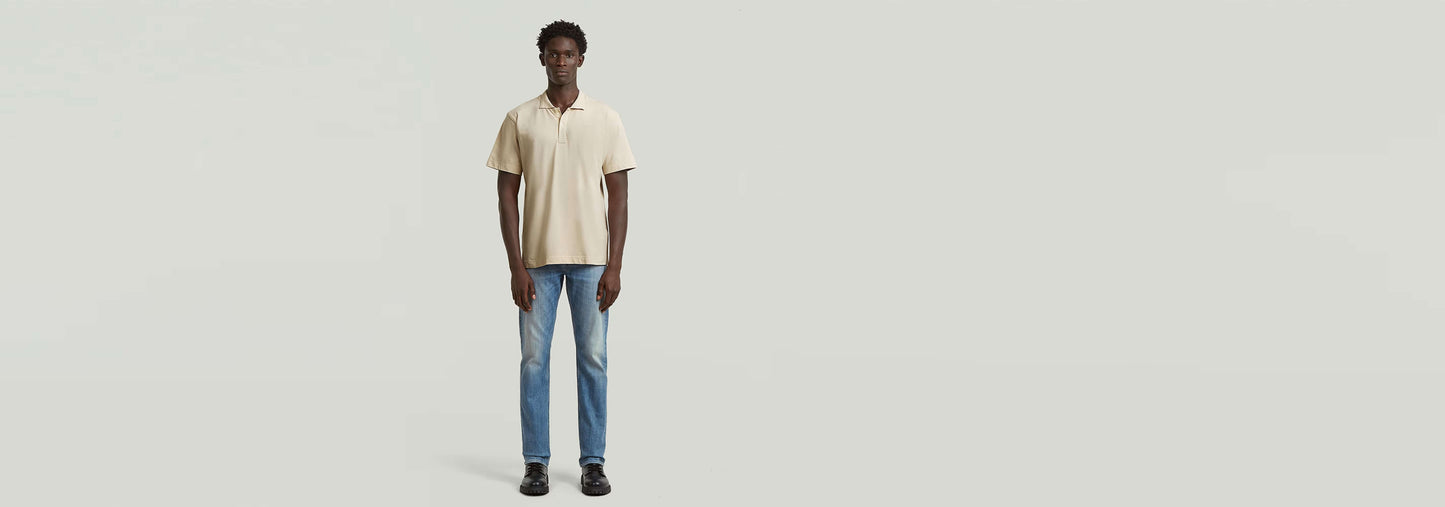 Hombre usando Polo Core Regular Jacquard en color crema con jeans azules, fondo gris claro.