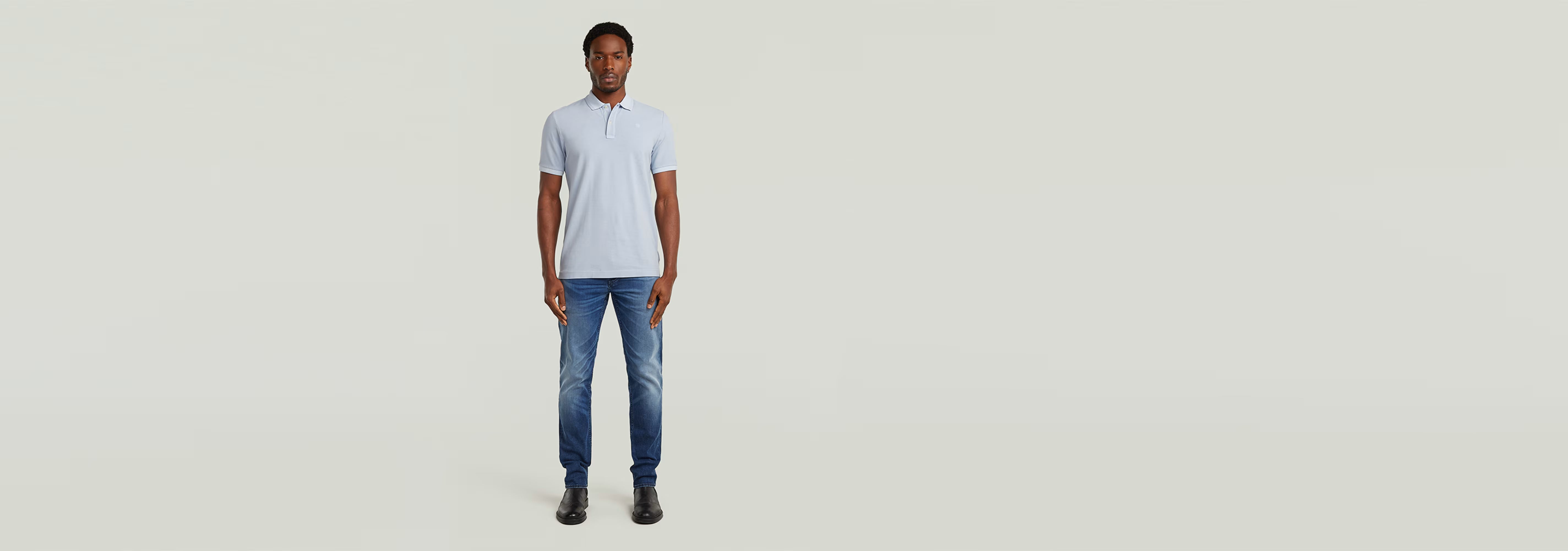 Modelo vistiendo el Polo Dunda Overdyed Slim en color claro, con jeans y zapatos, fondo minimalista.