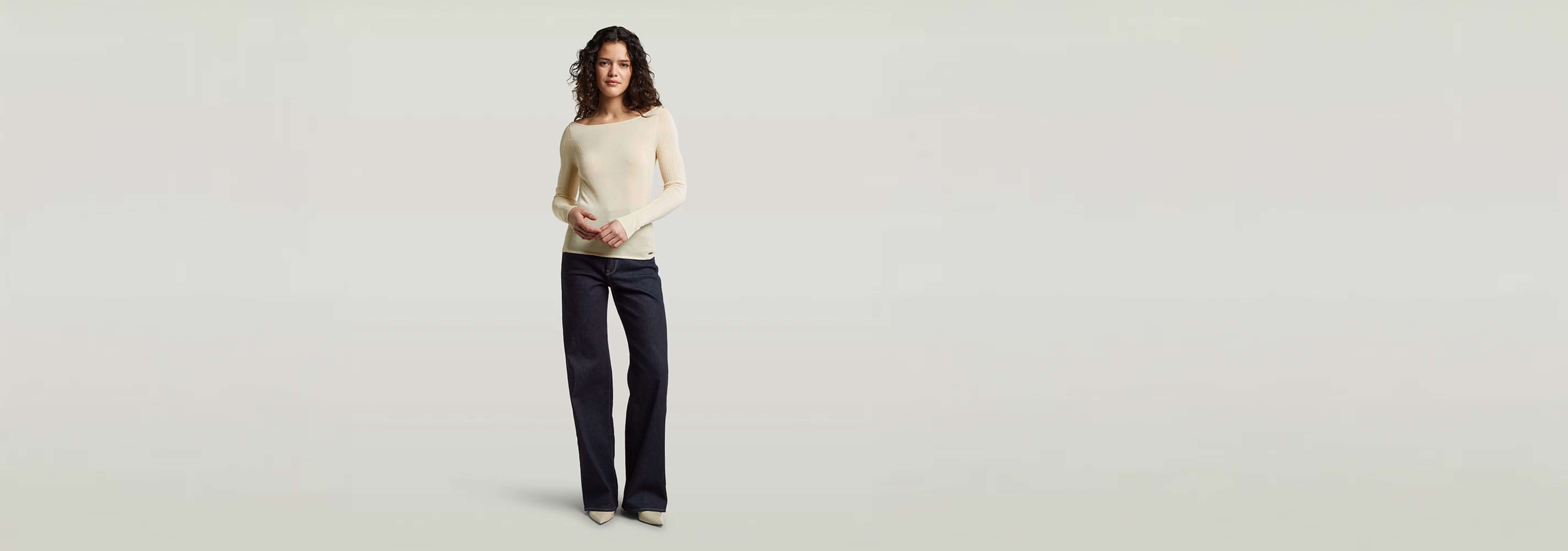 Mujer usando un suéter Punto ajustado Engineered Sheer con jeans, fondo neutro, estilo moderno y elegante.