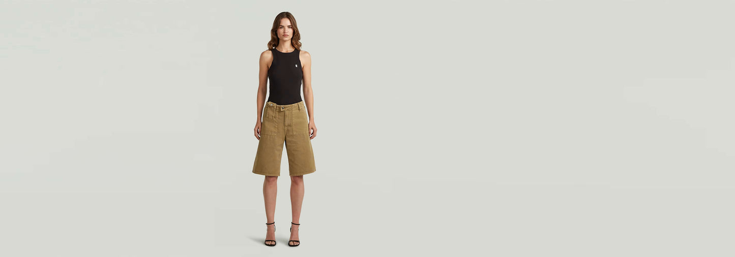 Mujer usando shorts Bermuda de ajuste ancho y cintura baja con camiseta negra y sandalias.