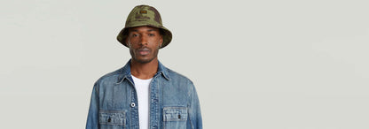 Hombre usando un Sombrero de pescador Originals con diseño de camuflaje y denim, luciendo moderno y casual.