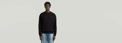 Hombre con sudadera GS-01 Relaxed en color negro, pantalones de mezclilla y fondo claro.
