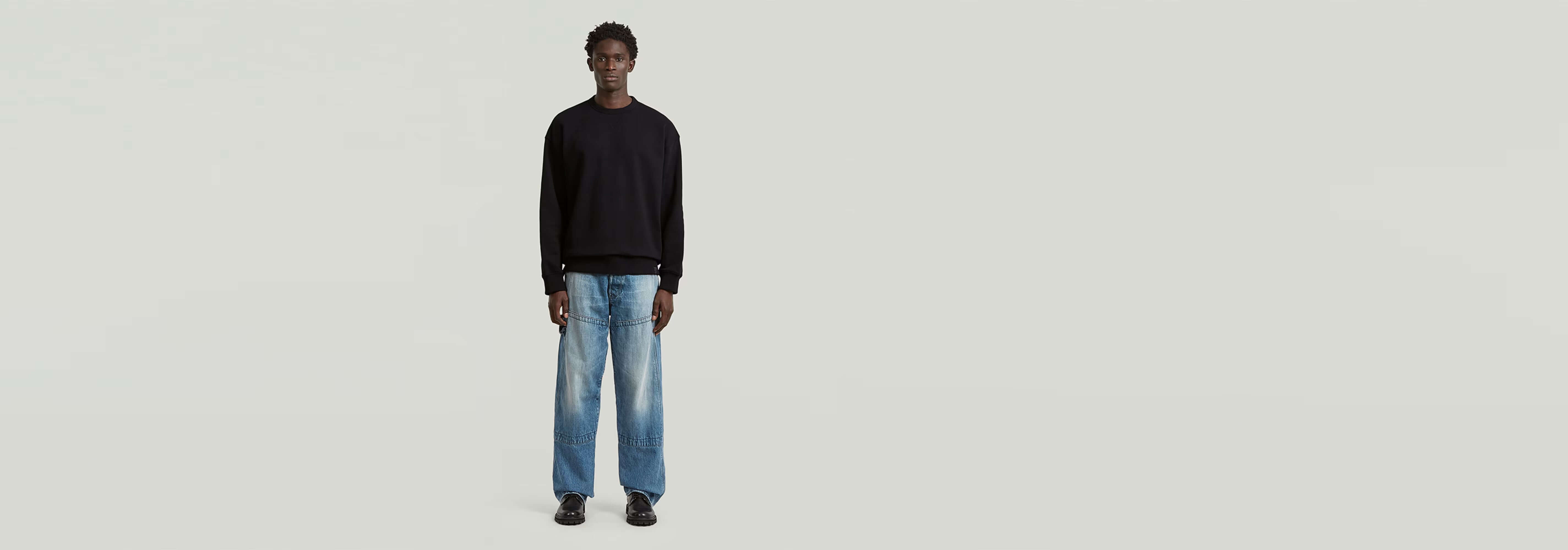 Modelo vistiendo la Sudadera GS-01 Relaxed en color negro, con jeans claros, fondo minimalista.