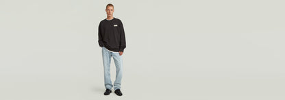 Hombre usando sudadera HB Badge de corte relajado, con jeans claros y zapatillas, fondo blanco.