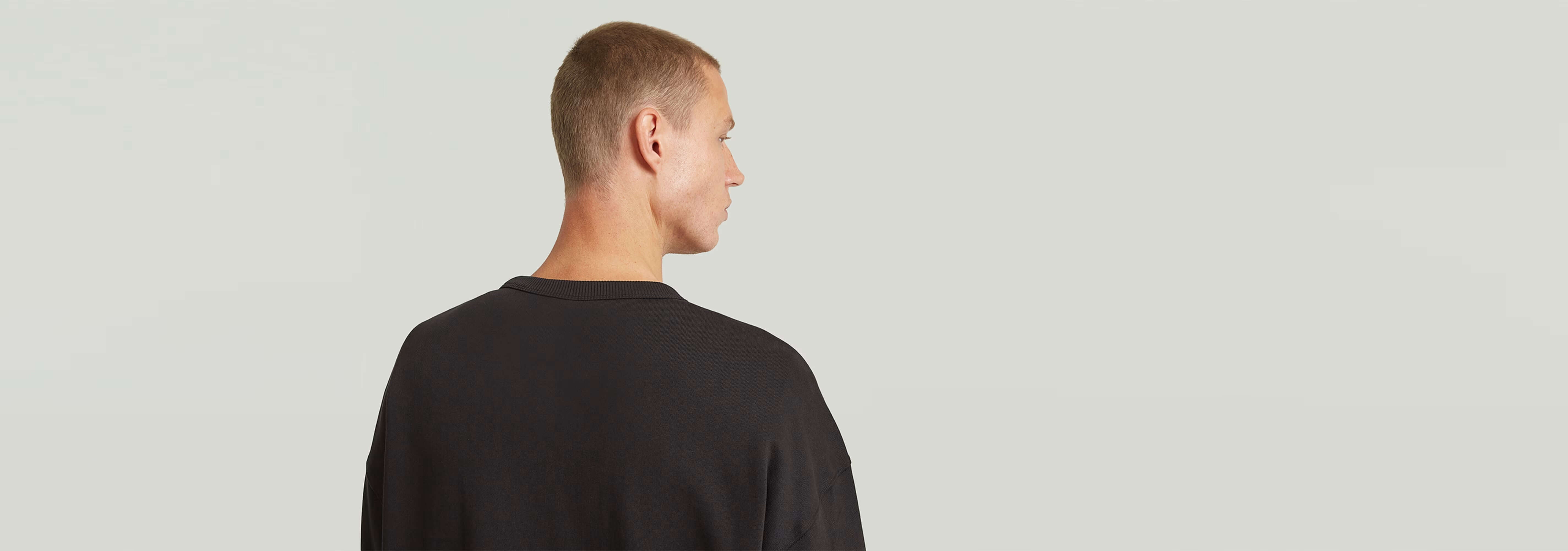 Hombre de espaldas luciendo la sudadera HB Badge, con corte relajado y diseño atractivo.
