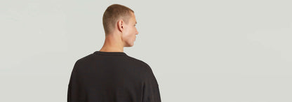 Hombre de espaldas luciendo la sudadera HB Badge, con corte relajado y diseño atractivo.