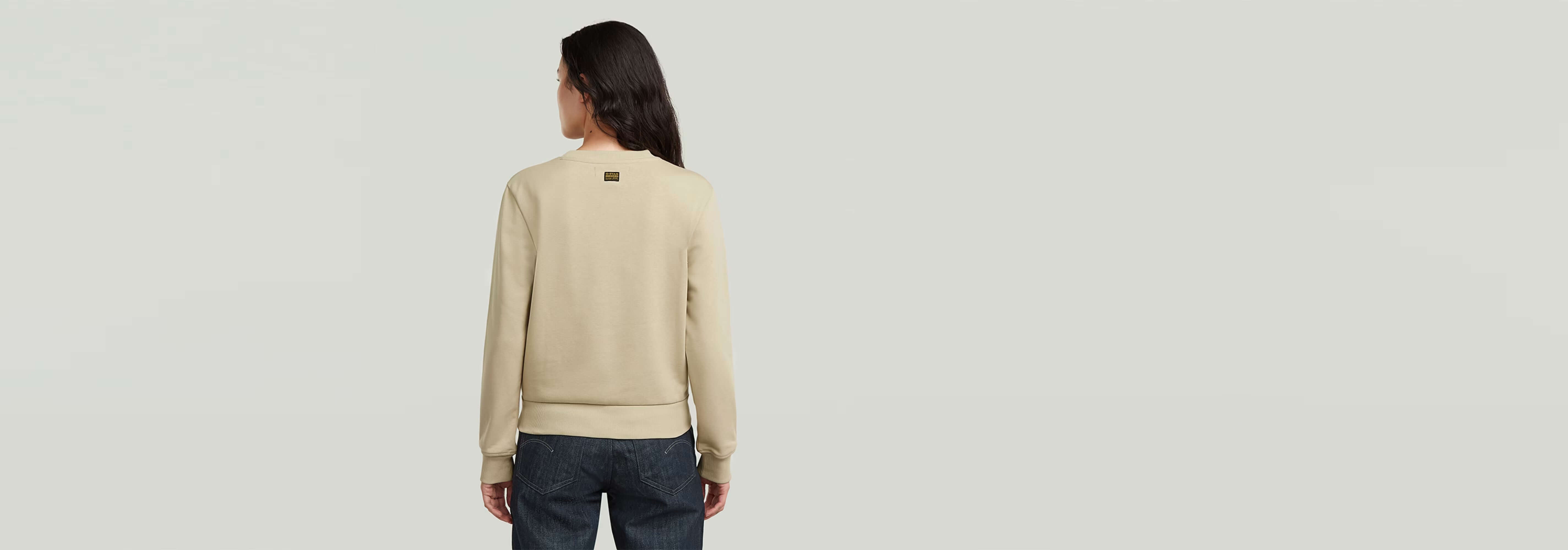 Mujer de espaldas viste el suéter Heritage Hardware Snaps en color beige con detalles en los bolsillos delanteros.
