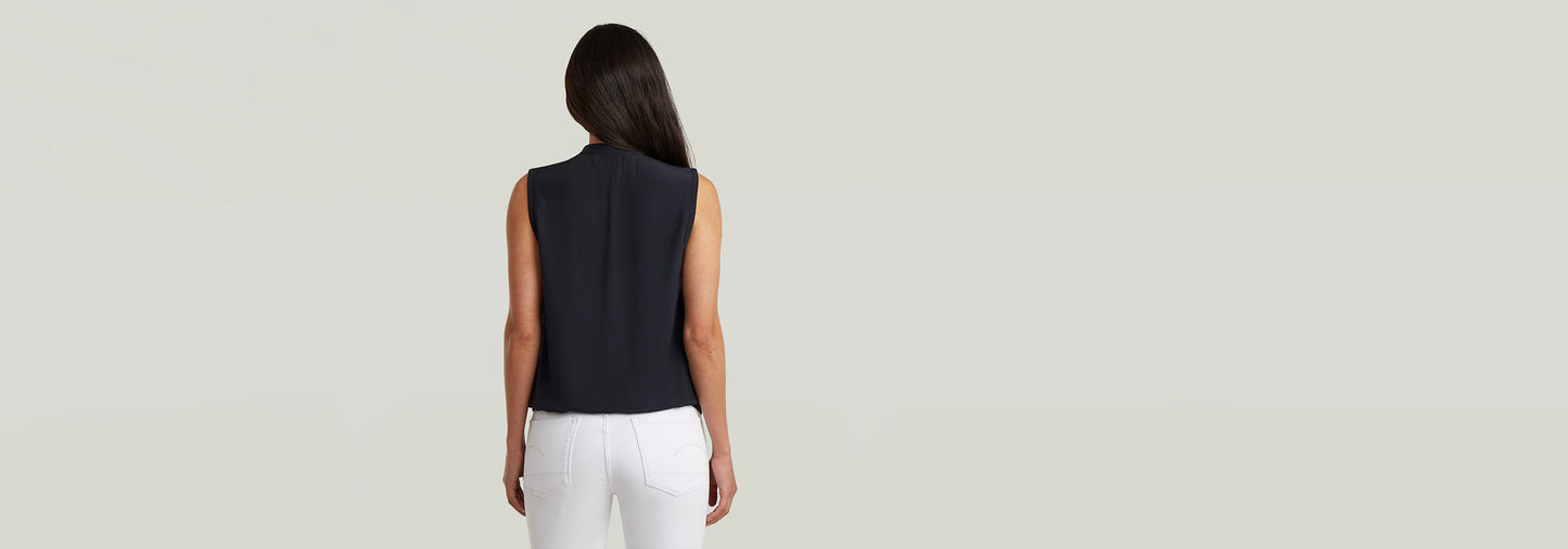 Mujer de espaldas luciendo el Top sin mangas Stand Up Collar en color negro con pantalones blancos.