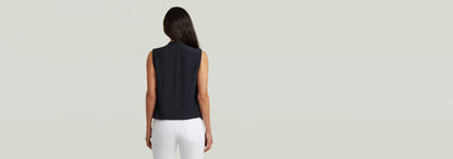 Mujer de espaldas luciendo el Top sin mangas Stand Up Collar en color negro con pantalones blancos.